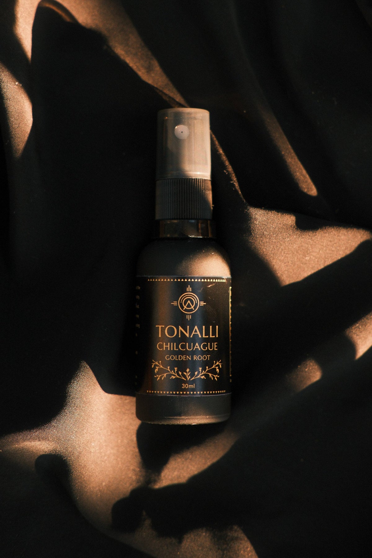 Tonalli Chilcuague Golden Root oral spray resting on dark fabric with gold dust