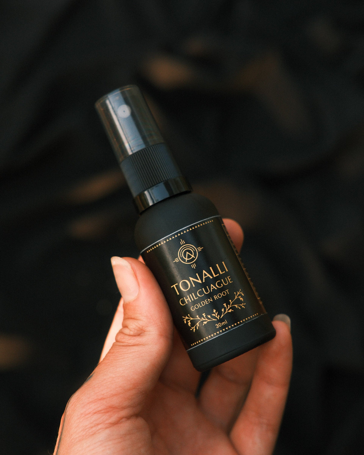 Tonalli Chilcuague oral spray held in hand against a dark backdrop